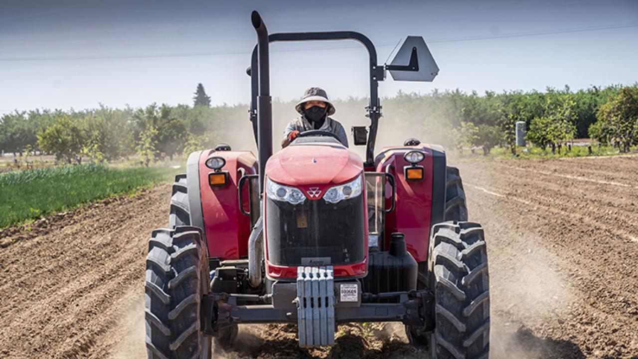 person wearing a hat and mask sit on a large tractor