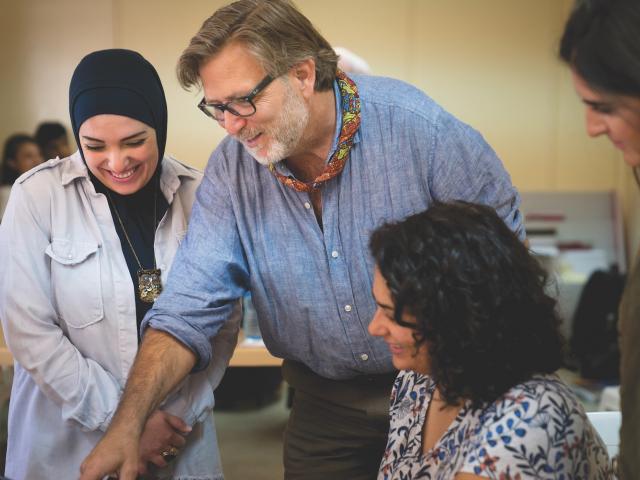     2. Man in a button up shirt points downward to something not pictured while three other individuals smile alongside him.